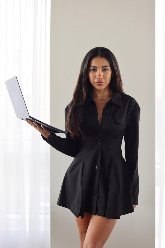 Naya standing with a laptop in a black dress